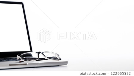 Closeup of an office table featuring a sleek laptop and reading glasses on a clean white surface Closeup of an office table featuring a sleek laptop and reading glasses on a clean white surface 122965552