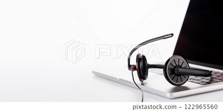 A sleek headset resting on a laptop, set against a bright white background A sleek headset resting on a laptop, set against a bright white background 122965560
