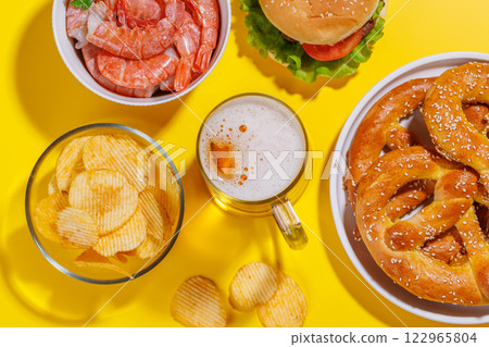 A vibrant photo showcasing a glass of beer surrounded by various snacks and fast food 122965804