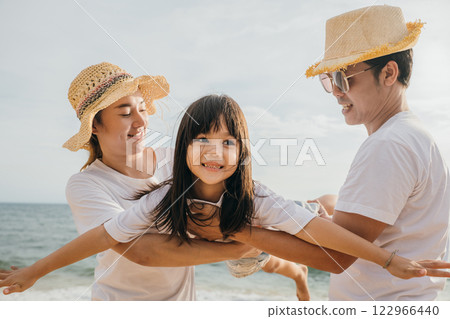 Asian family is playing together in fly action on the beach, Happy parents mother and father holding their child daughter spread arms out like airplane wings, family is enjoying their summer time 122966440