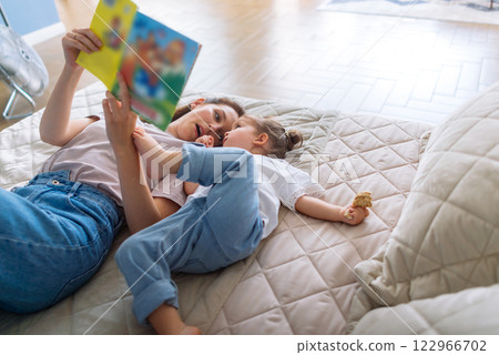 Little girl listens to her mom reading a book Little girl listens to her mom reading a book 122966702