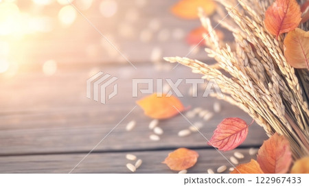A serene autumn scene featuring golden rice ears and scattered orange leaves on a rustic wooden surface 122967433