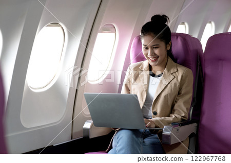 young businesswoman uses laptop while flying airplane for work young businesswoman uses laptop while flying airplane for work 122967768