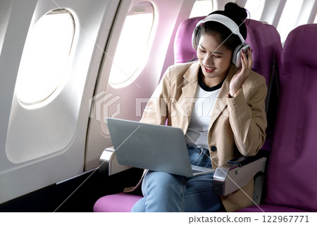 young woman is using a laptop and wireless headphones while traveling 122967771