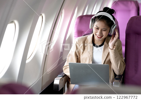 young woman is using a laptop and wireless headphones while traveling 122967772