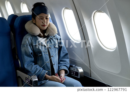 young woman travels alone on a plane and uses an eye mask young woman travels alone on a plane and uses an eye mask 122967791
