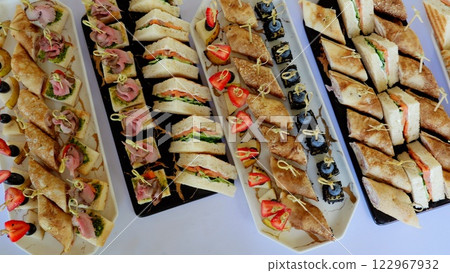 Varied platters holding delicate mini sandwiches, rolled crepes, and canapes, presenting sophisticated appetizers for professional catering service 122967932