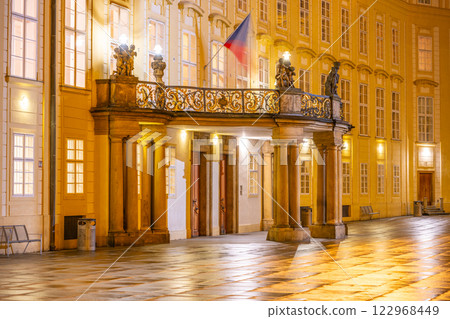 The grand entrance door of Prague Castle is illuminated as evening falls. The balcony adorned with statues and Czech flag adds charm to the architectural beauty of the Third Courtyard. The grand entrance door of Prague Castle is illuminated as evening falls. The balcony adorned with statues and Czech flag adds charm to the architectural beauty of the Third Courtyard. 122968449