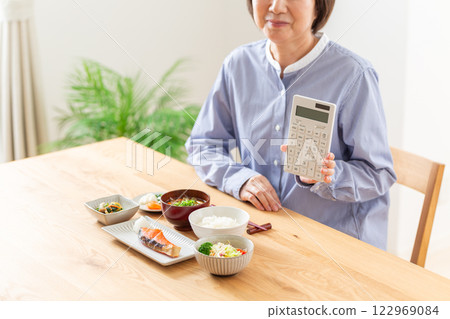 A middle-aged woman smiling and holding a calculator in front of a Japanese breakfast 122969084