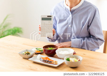 A middle-aged woman holding a calculator in front of a Japanese breakfast 122969125