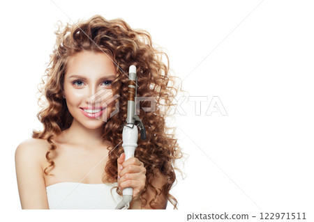 Charming brunette model using curling iron on white background.  122971511