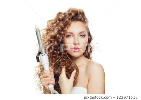 Gorgeous woman with curly hairstyle using hot curling tongs iron, indoor fashion portrait. Gorgeous woman with curly hairstyle using hot curling tongs iron, indoor fashion portrait. 122971513