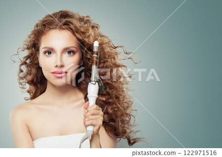 Gorgeous brunette model using curling iron on grey background.  122971516