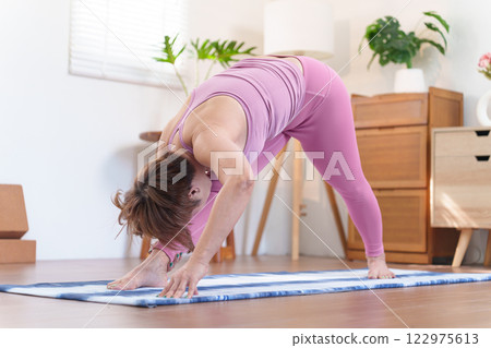 Senior Asian woman practicing Ardha Hanumanasana Half Splits Pose on a yoga mat in a cozy home setting Senior Asian woman practicing Ardha Hanumanasana Half Splits Pose on a yoga mat in a cozy home setting 122975613