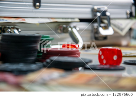 A red die and poker chips sit on a table beside a metal case 122976660