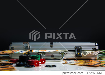 A silver aluminum case sits open on a white surface with stacks of cash and poker chips spilling out 122976661