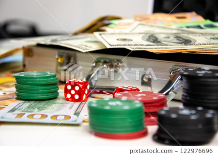 A close-up shot of a silver briefcase with red dice and stacks of casino chips and cash spilling out A close-up shot of a silver briefcase with red dice and stacks of casino chips and cash spilling out 122976696