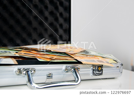 A close-up shot of a silver briefcase lying open on a white surface, revealing stacks of Euro bills inside A close-up shot of a silver briefcase lying open on a white surface, revealing stacks of Euro bills inside 122976697