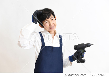 A middle-aged woman in a young apron having trouble while doing DIY A middle-aged woman in a young apron having trouble while doing DIY 122977669