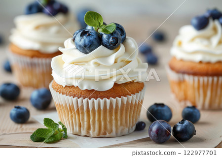 Freshly baked cupcake topped with creamy frosting, blueberries, and mint leaves. 122977701