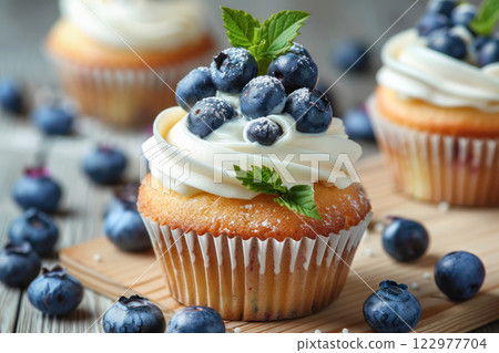 Freshly baked cupcake topped with creamy frosting, blueberries, and mint leaves. Freshly baked cupcake topped with creamy frosting, blueberries, and mint leaves. 122977704