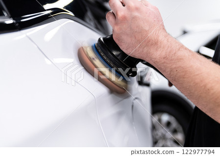 Car wash or detailing studio employee polishes white car paint, 122977794