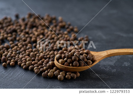 allspice or Jamaican pepper seeds in a wooden spoon on a black stone table, selective focus. 122979353