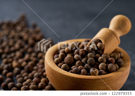allspice or Jamaican pepper seeds in a wooden bowl on a black stone table, selective focus. 122979355