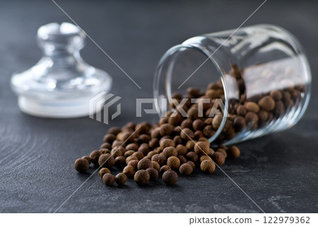 allspice or Jamaican pepper spill out of a glass storage jar on a black kitchen table, selective focus. allspice or Jamaican pepper spill out of a glass storage jar on a black kitchen table, selective focus. 122979362