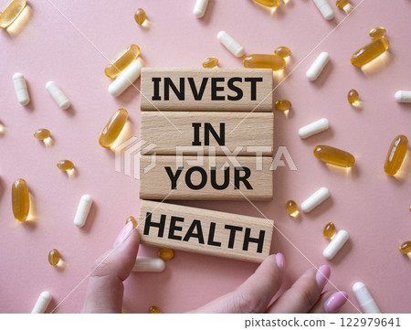 Invest in your Health symbol. Concept word Invest in your Health on wooden blocks. Businessman hand. Beautiful pink background with pills. Medicine concept. Copy space Invest in your Health symbol. Concept word Invest in your Health on wooden blocks. Businessman hand. Beautiful pink background with pills. Medicine concept. Copy space 122979641