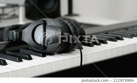 Headphones lie on the keys of the synthesizer. Headset on an electronic piano. Music creation and sound recording concept Headphones lie on the keys of the synthesizer. Headset on an electronic piano. Music creation and sound recording concept 122979904