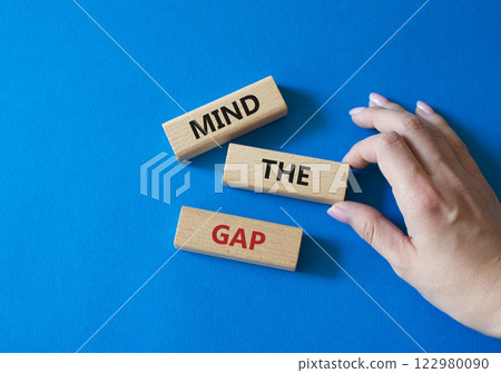 Mind the gap symbol. Concept words Mind the gap on wooden blocks. Beautiful blue background. Businessman hand. Business and Mind the gap concept. Copy space. Mind the gap symbol. Concept words Mind the gap on wooden blocks. Beautiful blue background. Businessman hand. Business and Mind the gap concept. Copy space. 122980090