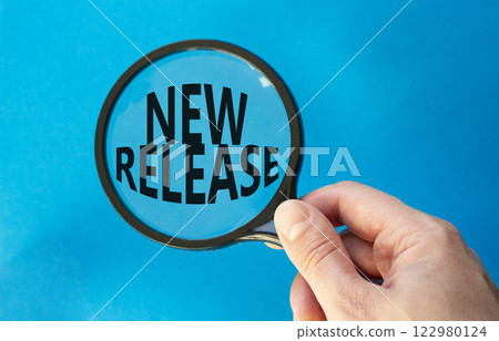 New Release symbol. Concept word New Release on magnifying glass. Beautiful blue background. Businessman hand. Business and New Release concept. Copy space. 122980124