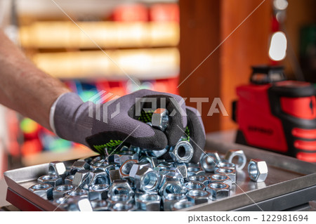 A closeup view of a hand meticulously sorting various metal bolts and nuts in a workshop setting 122981694