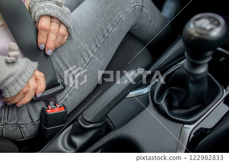 A female driver is fastening her seatbelt in a car, ensuring her safety on the road 122982833
