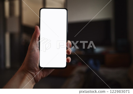 Man hold smartphone with white screen in his hand lying on a couch in home environment 122983071