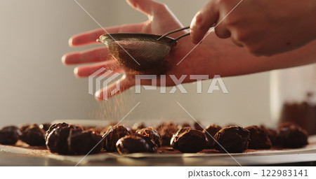 young woman sprinkle cocoa powder on chocolate truffles young woman sprinkle cocoa powder on chocolate truffles 122983141