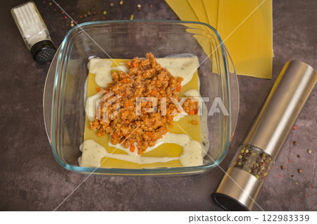 Bolognese sauce in a glass form. Lasagne pasta sheets, pepper mill, salt cellar. Black background. Homemade lasagna cooking preparation 122983339