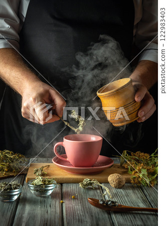 Hands carefully prepare a fragrant herbal tea in a charming kitchen, steam rising from the pink cup while fresh herbs and spices are delicately added to enhance the flavor and aroma Hands carefully prepare a fragrant herbal tea in a charming kitchen, steam rising from the pink cup while fresh herbs and spices are delicately added to enhance the flavor and aroma 122983403