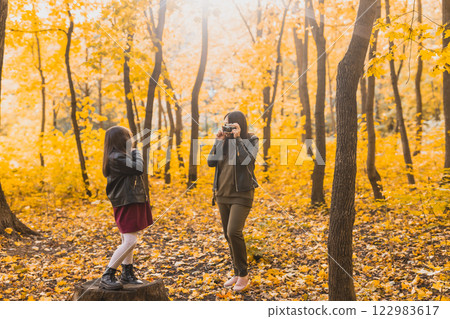 Mother taking picture her charismatic daughter on retro camera in autumn park. Hobbies and leisure concept. 122983617