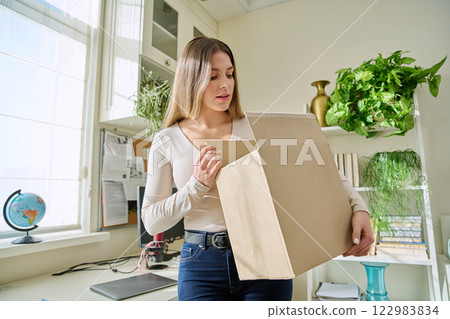 Young woman at home unpacks cardboard box with online purchases Young woman at home unpacks cardboard box with online purchases 122983834
