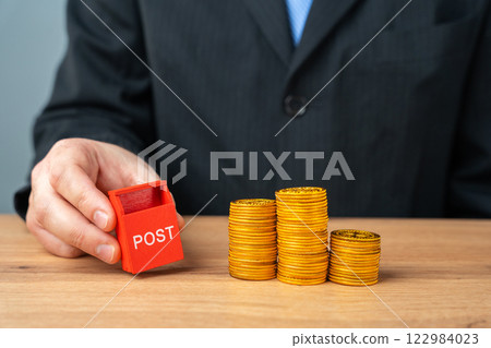 Mailbox figurine in businessman's hands and coins. Parcel delivery and transportation concept. Logistics and economics Mailbox figurine in businessman's hands and coins. Parcel delivery and transportation concept. Logistics and economics 122984023