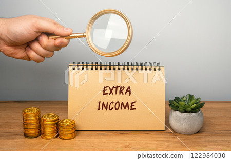Extra income concept. Money earned in addition to a primary source of income, such as a salary or wages. notebook, magnifying glass and coins 122984030