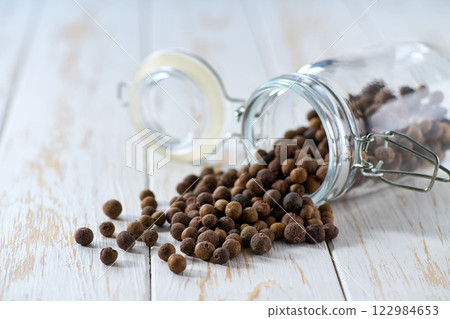 allspice or Jamaican pepper spill out of a glass storage jar on a light kitchen table, selective focus. 122984653
