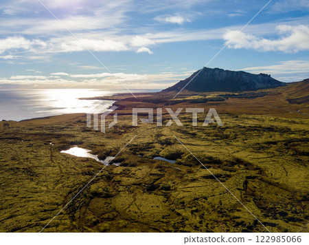 Aerial perspective of the snaefellsnes peninsula, iceland, illuminated by sunshine, highlighting its varied terrain of mossy lava fields, dramatic coastlines, and grand mountains Aerial perspective of the snaefellsnes peninsula, iceland, illuminated by sunshine, highlighting its varied terrain of mossy lava fields, dramatic coastlines, and grand mountains 122985066