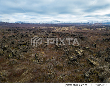 Beautiful aerial of the landscape featuring Dimmuborgir lava formations and snow-capped mountains in Iceland under a cloudy sky 122985085
