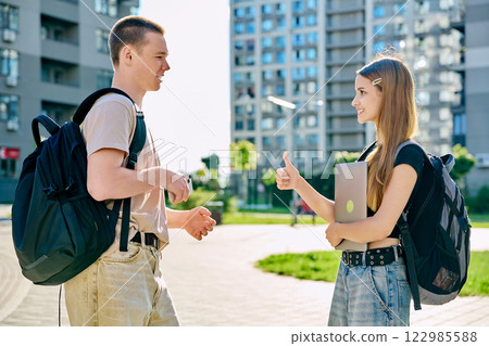 College students teenagers guy and girl with backpacks talking together, outdoor College students teenagers guy and girl with backpacks talking together, outdoor 122985588