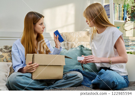 Two young females with cardboard box unpacking an online purchase from internet store Two young females with cardboard box unpacking an online purchase from internet store 122985594