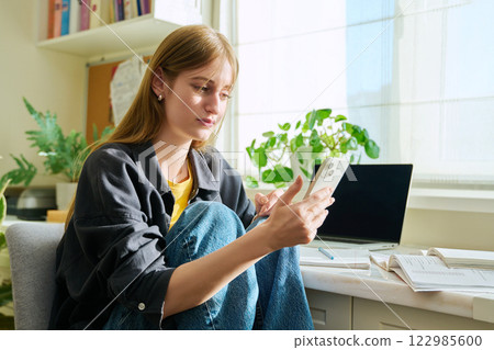 Serious teenage female sitting at home reading texting on smartphone 122985600