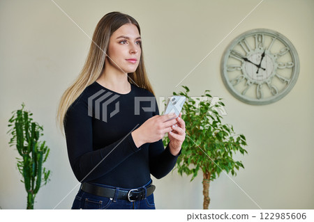 Young serious woman using smartphone standing at home Young serious woman using smartphone standing at home 122985606
